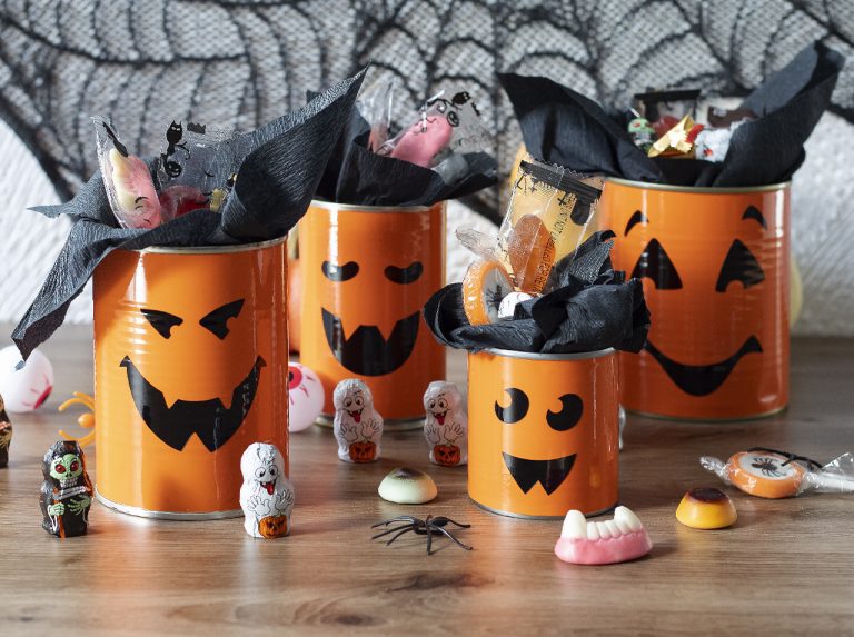 Upcycling DIY: Tin cans with d-c-fix® adhesive foils orange and black in the look of Halloween pumpkins with faces.