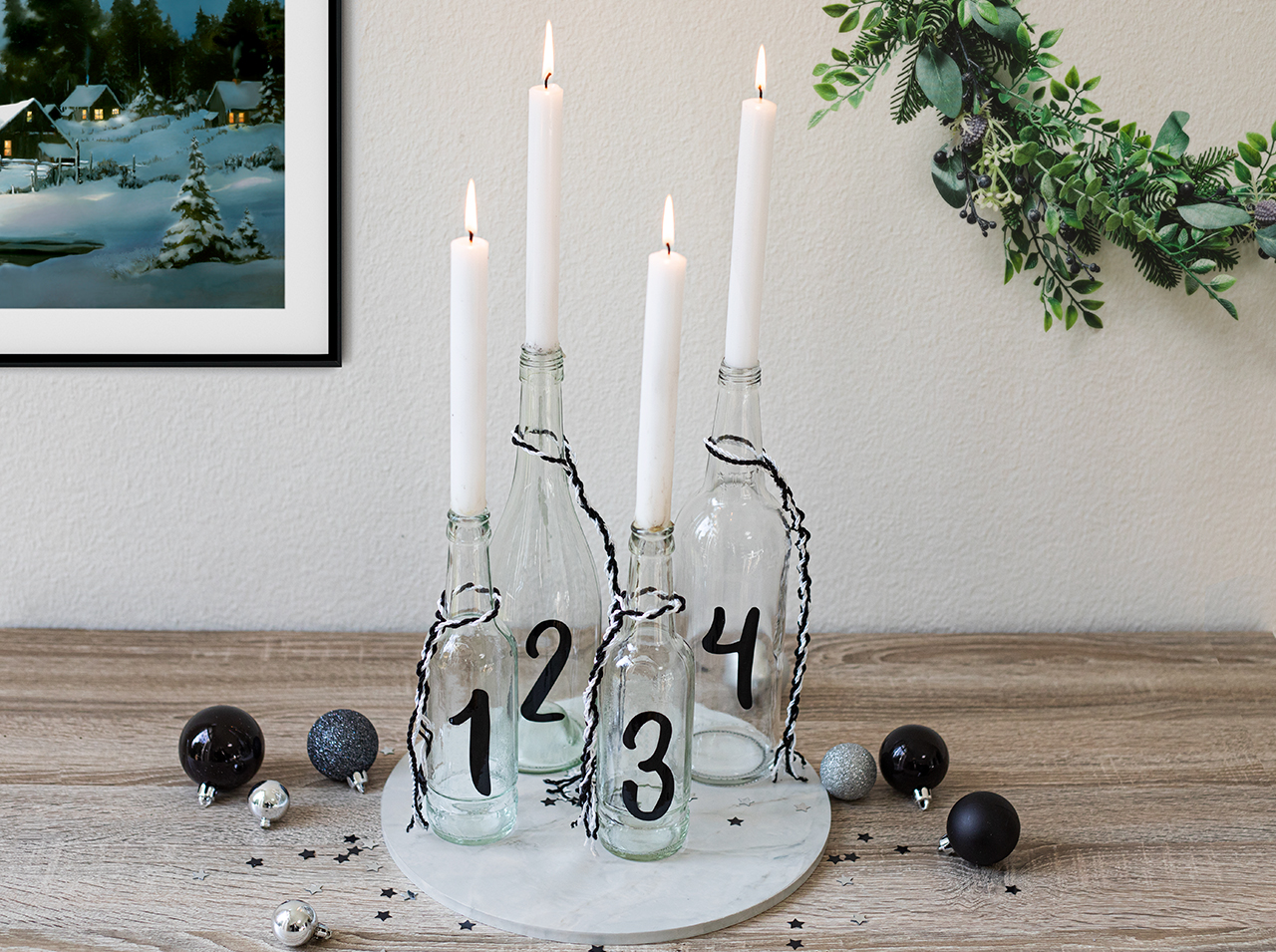 Modern DIY upcycling Advent wreath with candles in glass bottles on a round marble-effect base.