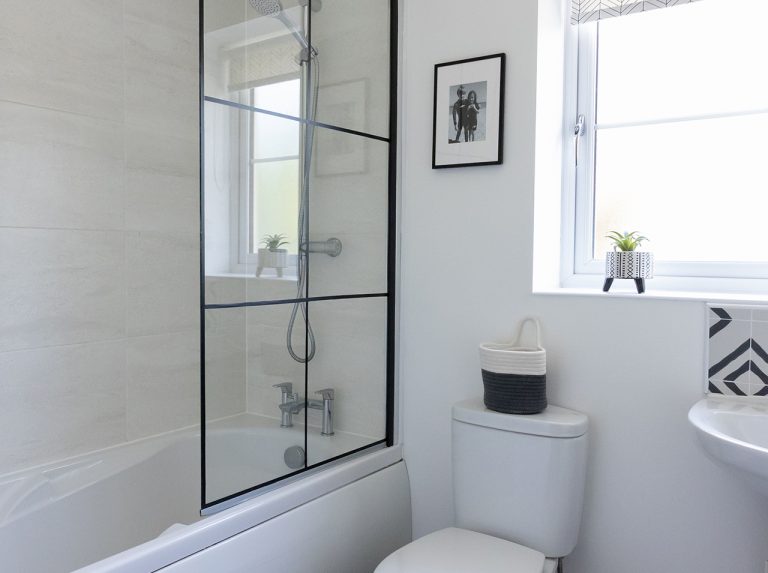 Ścianka kabiny prysznicowej w łazience, ze szkła, z ramką z czarnych pasków folii samoprzylepnej.