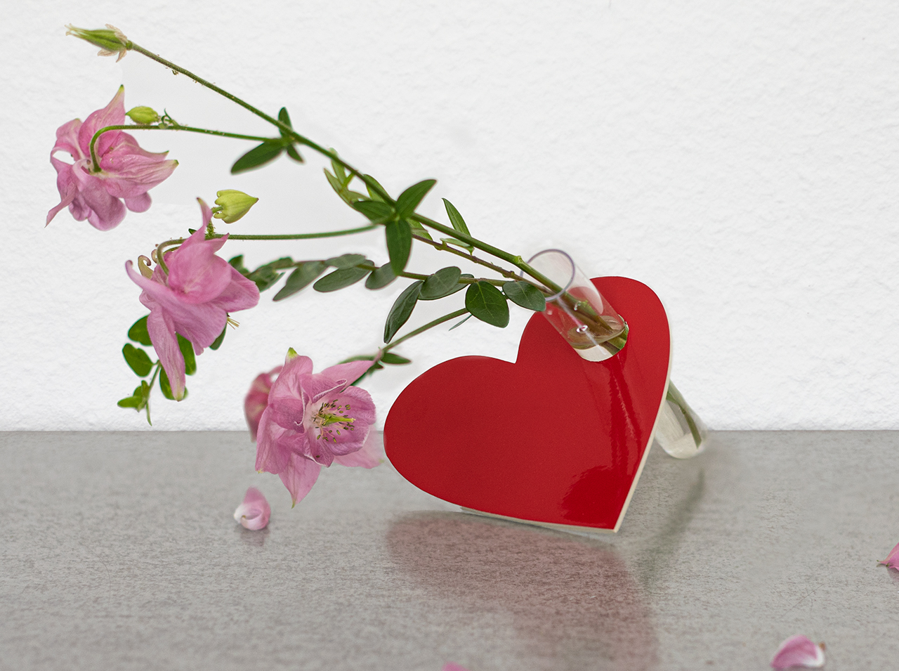 Serce wykonane ze sklejki pokrytej folią w kolorze czerwieni sygnałowej z małą probówką w środku, ozdobione świeżymi kwiatami.