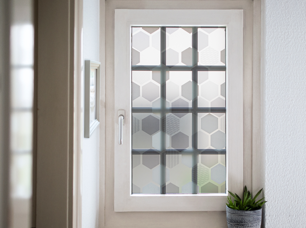 Okno oklejone nieprzezroczystą folią okienną z wzorem plastra miodu w kolorach białym, szarym i miętowym.