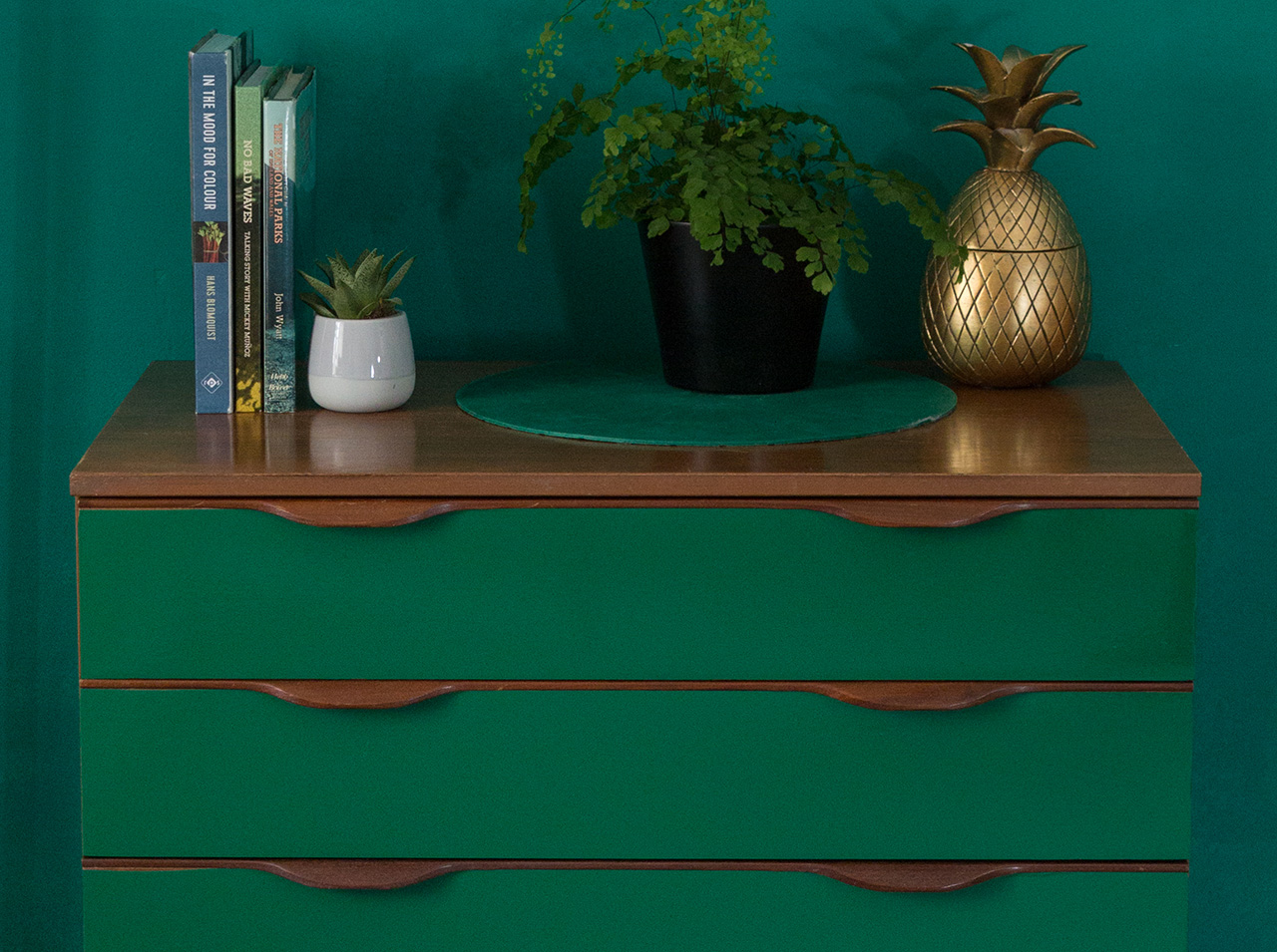 Komoda zaprojektowana przy użyciu folii samoprzylepnej w kolorze szmaragdowym, ustawiona na tle zielonej ściany.
