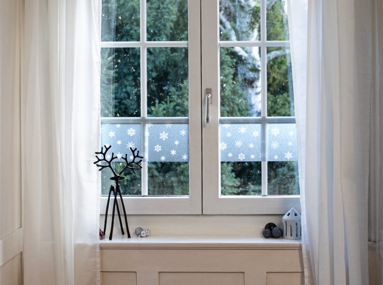 Fensterscheibe mit milchiger Fensterfolie mit Schneeflocken-Dekor in Weiß beklebt.