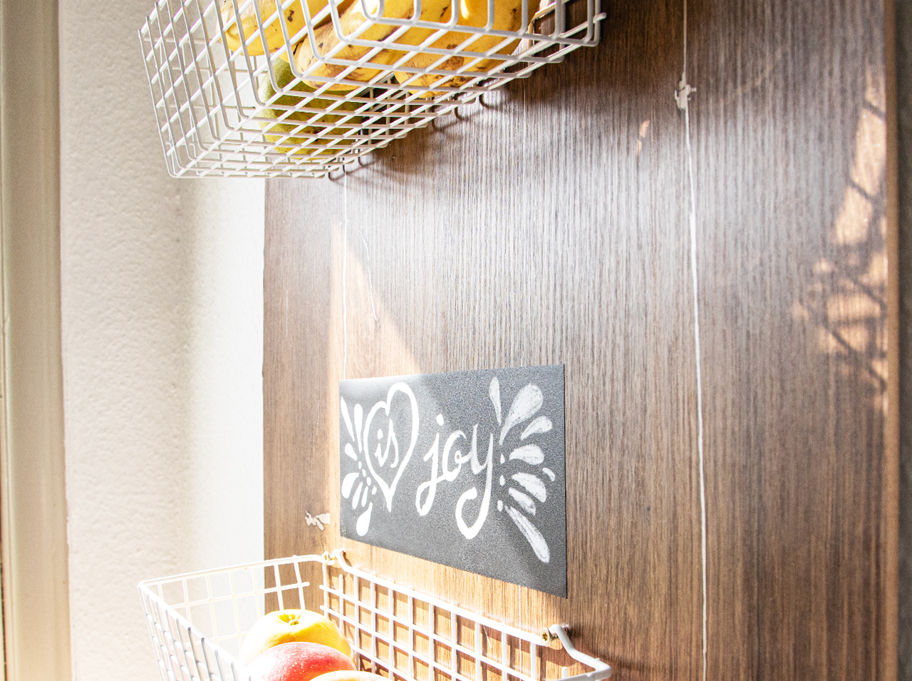 Board for the kitchen wall with a dark wood effect and mounted metal mesh baskets.
