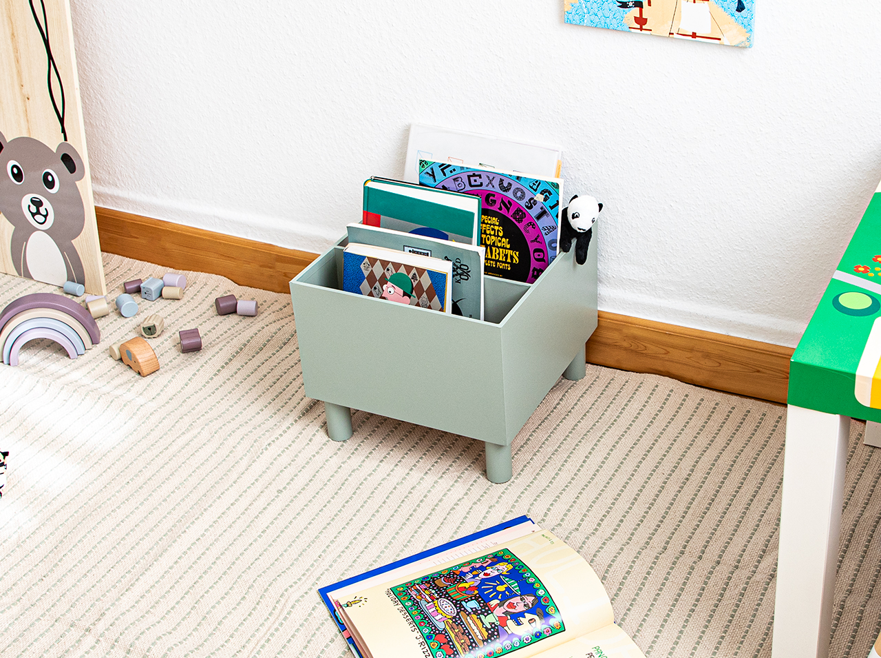Ikea Moppe dresser covered with adhesive foil in sage green with function as a open-top storage file on legs for children’s books.