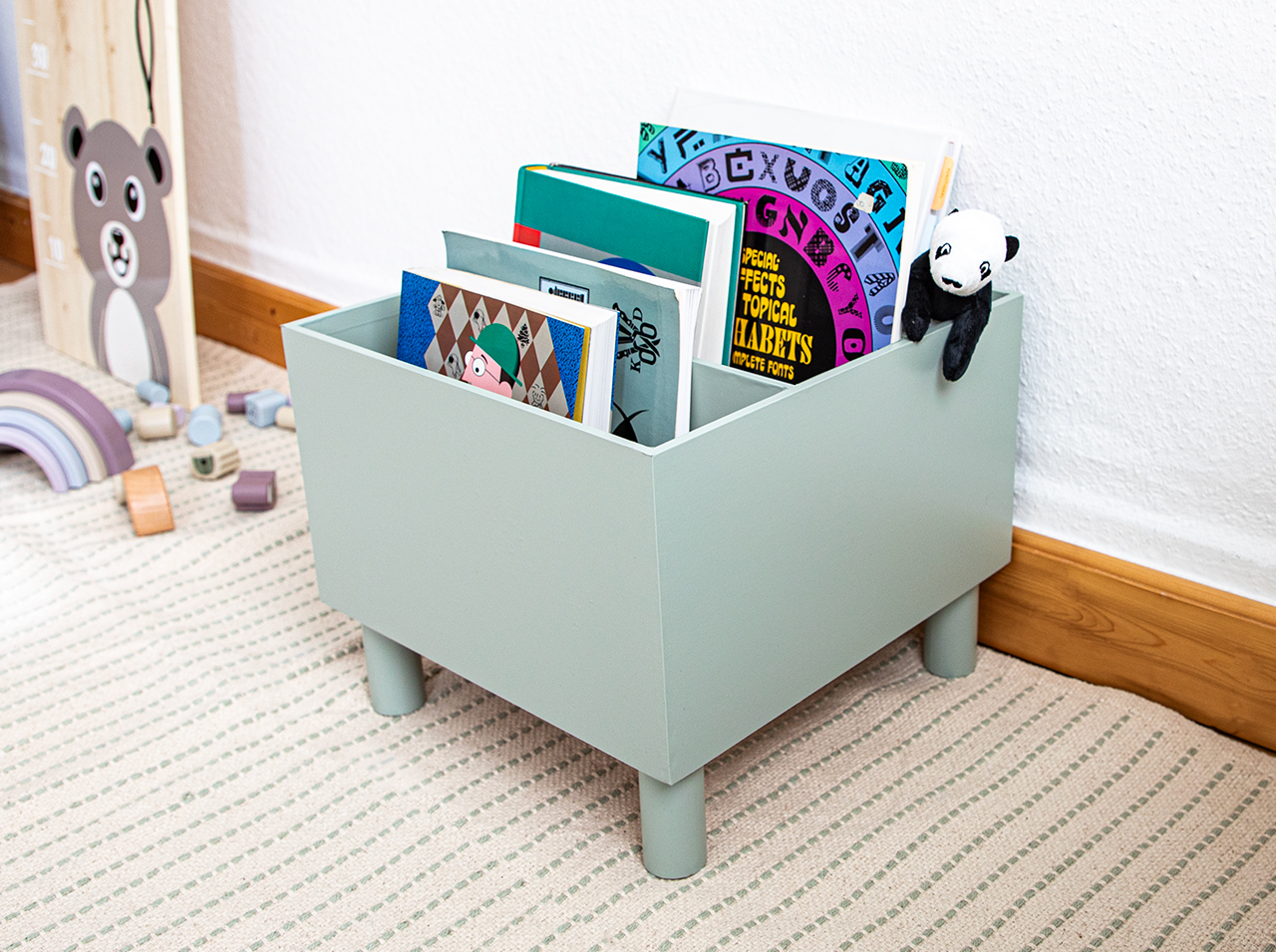 Ikea Moppe dresser covered with adhesive foil in sage green with function as a open-top storage file on legs for children’s books.