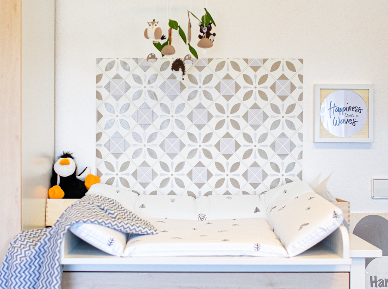 Above a dresser with a changing table attachment is wall paneling with an ornamental tile pattern in beige.
