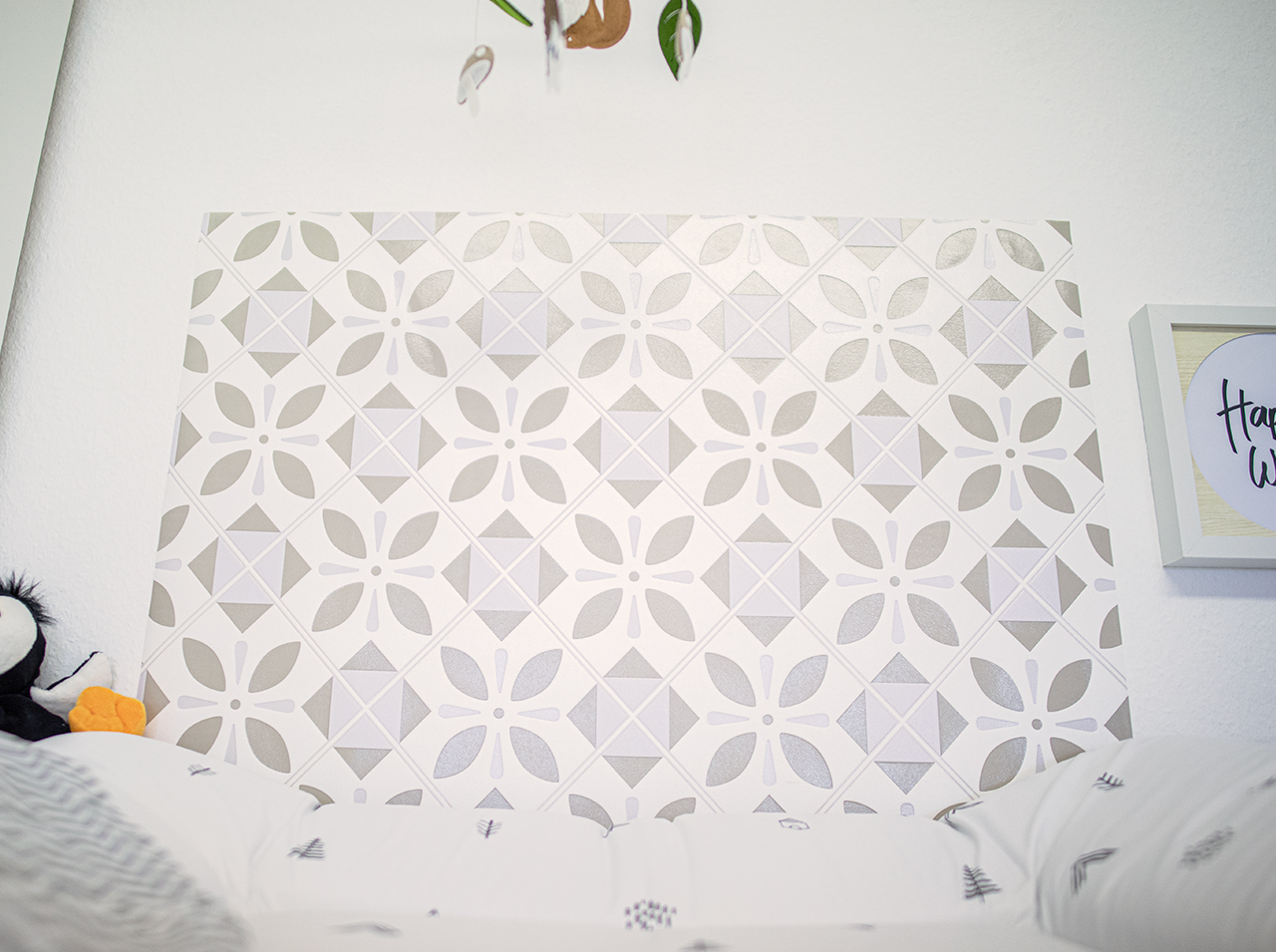 Above a dresser with a changing table attachment is wall paneling with an ornamental tile pattern in beige.