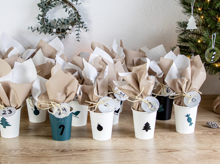Des gobelets blancs en carton, décorés aux couleurs de Noël, avec une surprise à l’intérieur, dans une serviette en papier nouée.